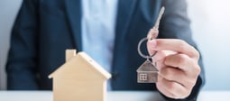 vecteezy_businessman-hand-holding-key-with-wooden-home-model-real_6694257