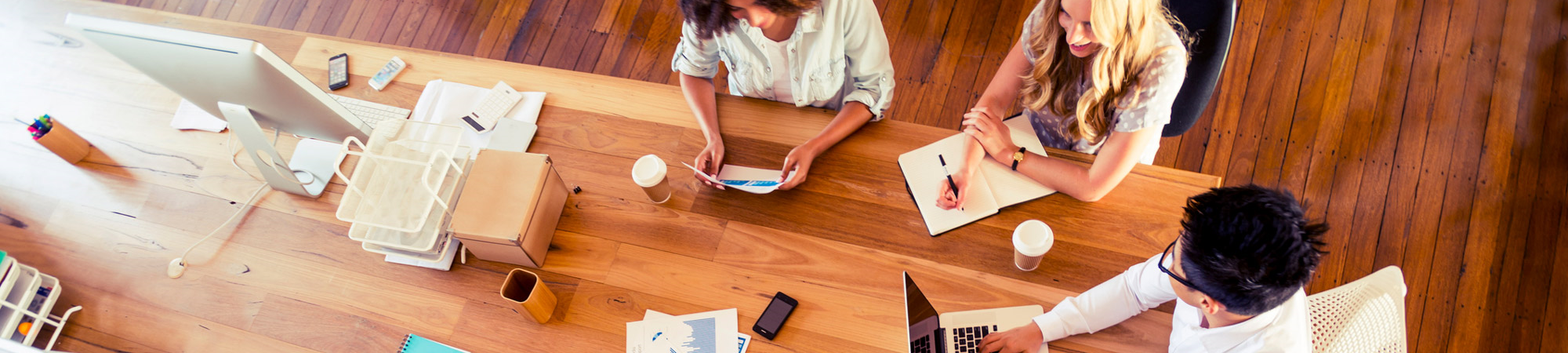 Three people working at a wooden desk Three people working at a wooden desk